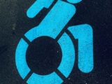 Close-up of a blue wheelchair symbol painted on a dark asphalt surface, highlighting accessibility.